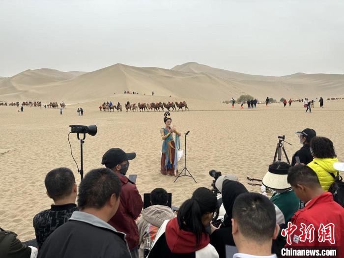 圖為2023年4月底，敦煌大漠“逐舞者”奧楠在鳴沙山月牙泉景區(qū)視頻直播，吸引游人圍觀。　馮志軍 攝